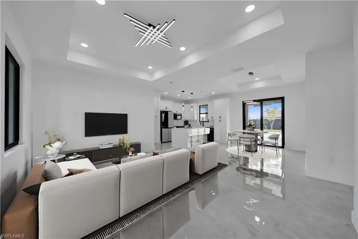 Living area with a raised ceiling, recessed lighting, and light marble finish flooring