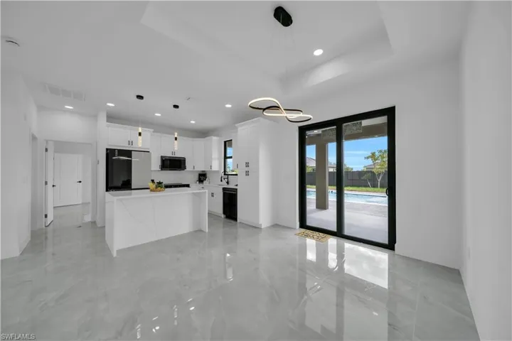 Kitchen with refrigerator, black microwave, white cabinetry, light marble finish flooring, and a center island