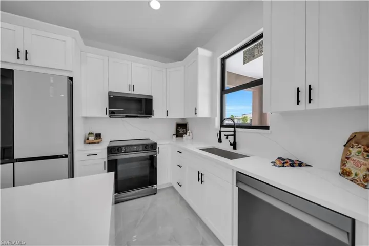 Kitchen with stainless steel appliances, light marble finish flooring, and white cabinets