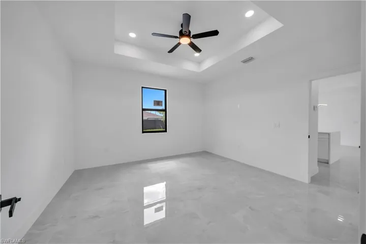 Empty room with recessed lighting, light marble finish floors, ceiling fan, and a tray ceiling