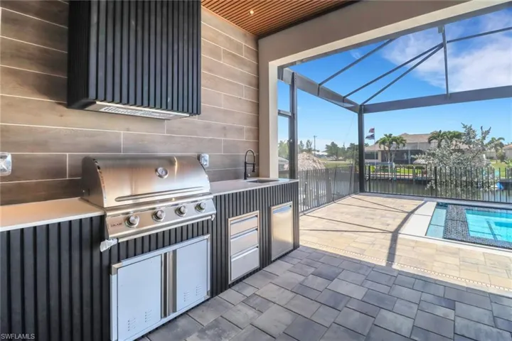 Outdoor kitchen with stainless steel refrigerator, gas grill and range hood