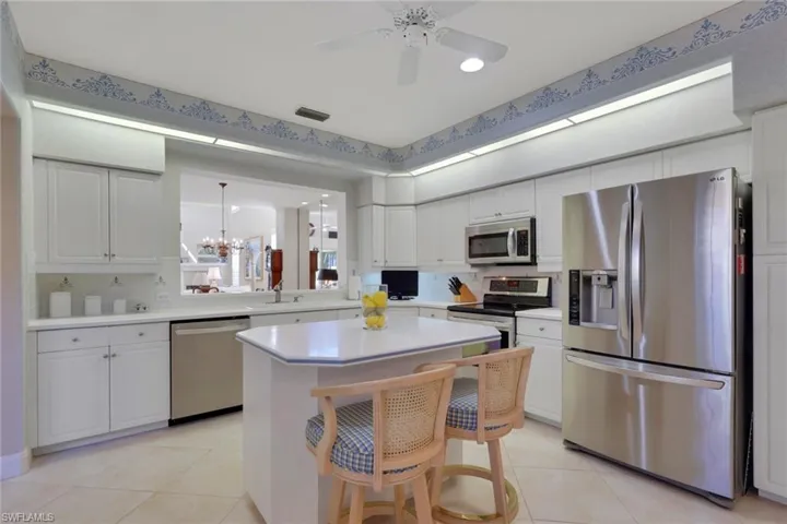 Kitchen with appliances with stainless steel finishes, white cabinets, light countertops, a kitchen bar, and a chandelier