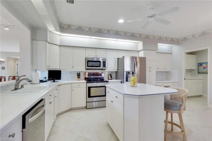 Kitchen with a breakfast bar, stainless steel appliances, white cabinets, light countertops, and recessed lighting