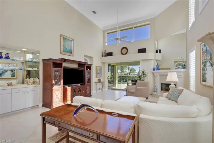 Living area with a fireplace, crown molding, a ceiling fan, light tile patterned floors, and a towering ceiling