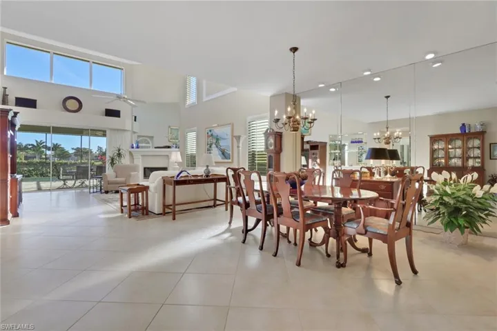 Dining room with a fireplace, ceiling fan, a chandelier, light tile patterned floors, and a towering ceiling