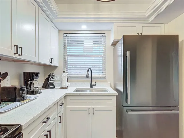 Kitchen with stainless steel fridge, sink, ornamental molding, and white cabinets