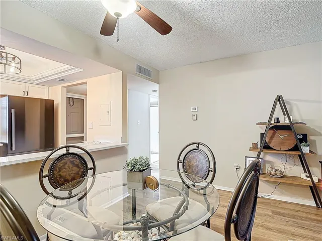 Dining space with light hardwood / wood-style floors, a textured ceiling, ceiling fan, and a tray ceiling