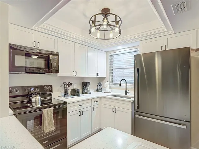 Kitchen with white cabinets, black appliances, sink, crown molding, and a raised ceiling
