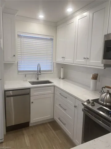 Kitchen featuring sink, stainless steel appliances, white cabinetry, and decorative backsplash