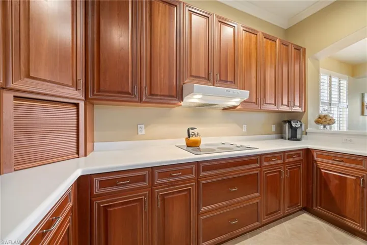 Kitchen with light countertops, ornamental molding, light tile patterned floors, wood finish cabinetry, and electric stovetop