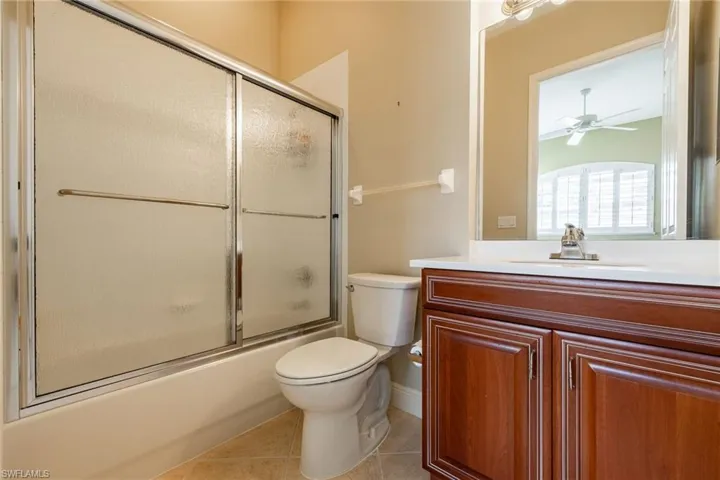 Bathroom with bath / shower combo with glass door, vanity, light tile patterned floors, and ceiling fan