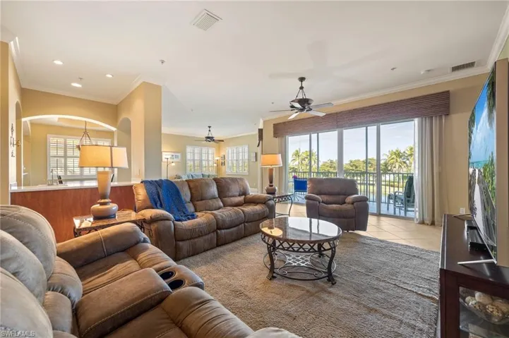 Tiled living area with ornamental molding, arched walkways, and a ceiling fan