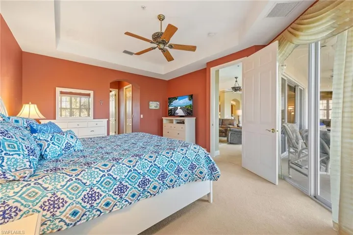 Bedroom with arched walkways, access to exterior, light colored carpet, ceiling fan, and a raised ceiling