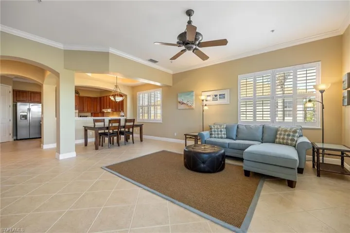Living area with arched walkways, light tile patterned flooring, crown molding, and ceiling fan
