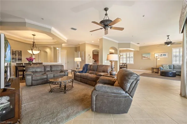 Living room with a raised ceiling, arched walkways, crown molding, tile patterned flooring, and a ceiling fan