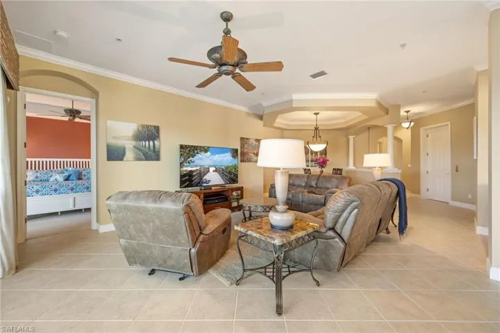 Living area featuring a ceiling fan, ornamental molding, a tray ceiling, light tile patterned floors, and arched walkways