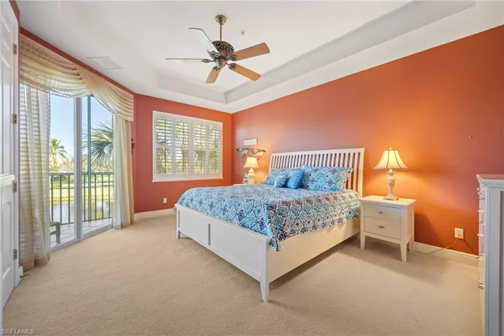 Bedroom featuring carpet flooring, access to outside, a tray ceiling, and a ceiling fan