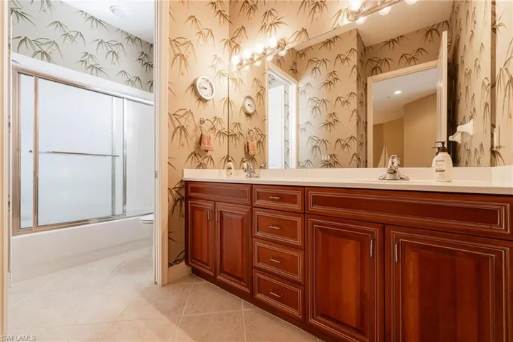 Full bathroom with double vanity, enclosed tub / shower combo, and light tile patterned flooring