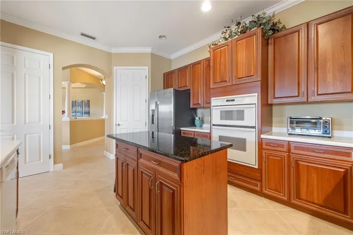 Kitchen with arched walkways, white appliances, wood finish cabinets, light tile patterned floors, and a center island