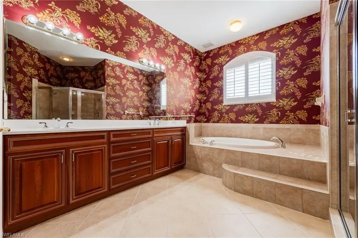 Bathroom with a stall shower, double vanity, a bath, light tile patterned flooring, and wallpapered walls