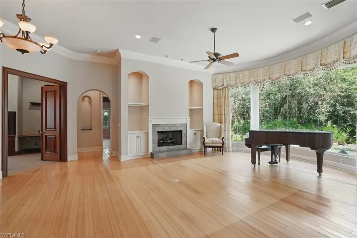 Living area featuring ornamental molding, light wood-style flooring, ceiling fan, arched walkways, and built in shelves