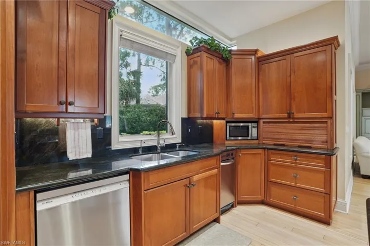 Kitchen featuring appliances with stainless steel finishes, a sink, decorative backsplash, dark stone countertops, and light wood-style flooring