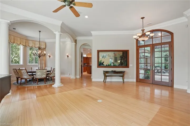 Living area featuring a chandelier, arched walkways, ornate columns, light wood-style flooring, and french doors