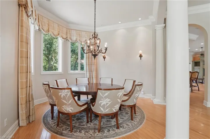 Dining space featuring decorative columns, ornamental molding, light wood finished floors, a chandelier, and baseboards