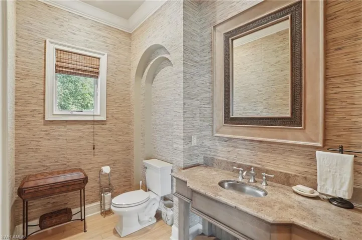 Half bathroom featuring ornamental molding, toilet, vanity, and wood finished floors