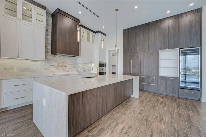 Kitchen featuring two tone color scheme, light stone counters, a kitchen island with sink, glass insert cabinets, and wood tiled floors