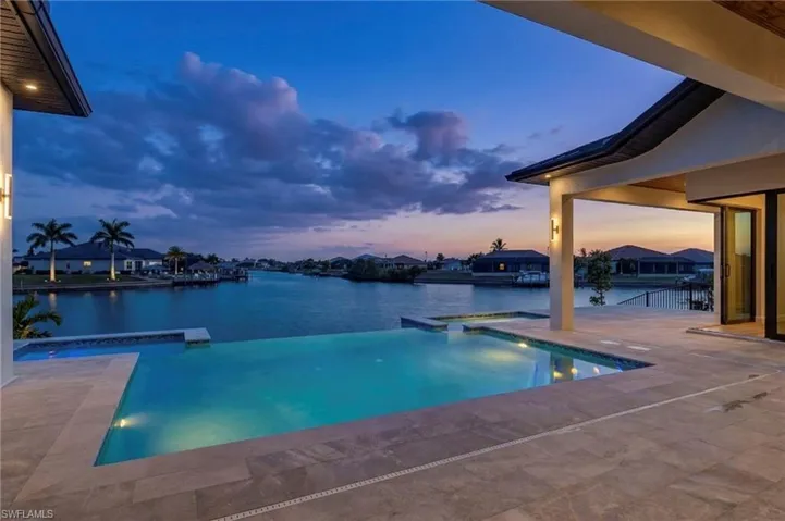 Pool at dusk featuring a patio area, a pool with connected hot tub, and a water view