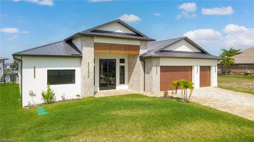 View of front facade with a standing seam roof, a front yard, a garage, driveway, and stucco siding