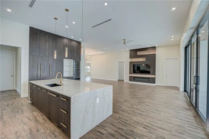 Kitchen with modern cabinets, dark wood finish cabinets, light stone counters, and a center island with sink