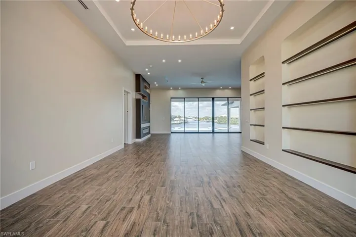 Unfurnished living room with dark wood-type flooring, built in shelves, and a chandelier