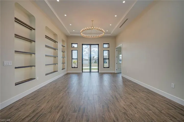 Unfurnished room with built in features, a raised ceiling, suspended lighting, and dark wood-type flooring