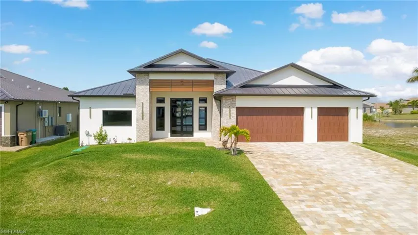 View of front of property with a standing seam roof, an attached garage, driveway, a front lawn, and stucco siding
