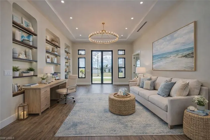 Office space featuring dark wood-style floors, a raised ceiling, suspended lighting, built in desk, and built in shelves