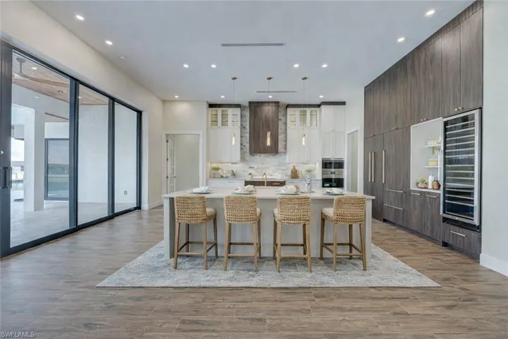 Two tone kitchen with dual tone cabinetry, a breakfast bar area, a large island with sink, wine cooler, and modern cabinets