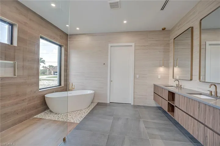 Full bathroom with tile walls, double vanity, a freestanding bath, dark tile patterned flooring, and recessed lighting