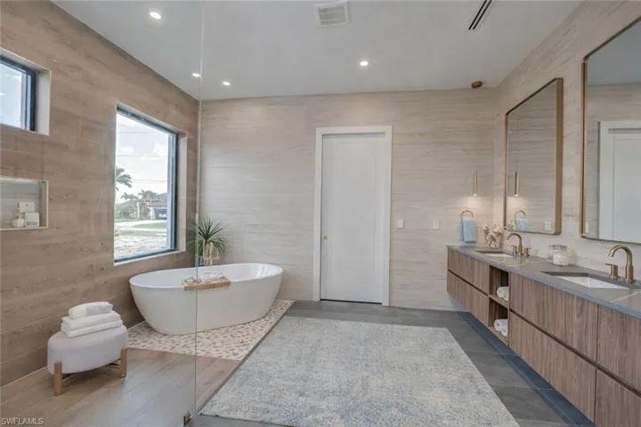 Full bathroom with double vanity, a soaking tub, tile walls, and recessed lighting