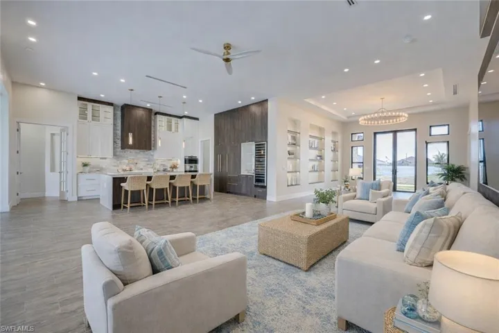 Living room with a ceiling fan, light wood-style floors, hanging lights, wine cooler, and a tray ceiling