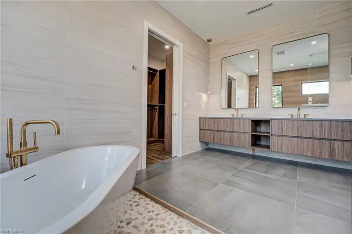 Full bathroom featuring tile walls, double vanity, a soaking tub, dark tile patterned floors, and a walk in closet