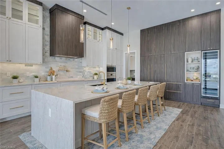Dual tone kitchen featuring light stone countertops, wine cooler, dark wood finished floors, a kitchen bar, and glass insert cabinets