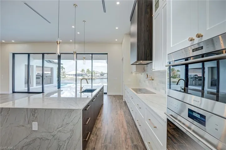 Dual tone kitchen featuring double oven, light stone counters, dual tone cabinets, pendant lighting, and dark wood-style floors