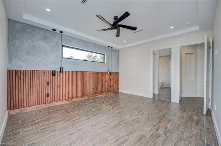 Spare room with wooden walls, wood tiled floors, a raised ceiling, a ceiling fan, and wainscoting