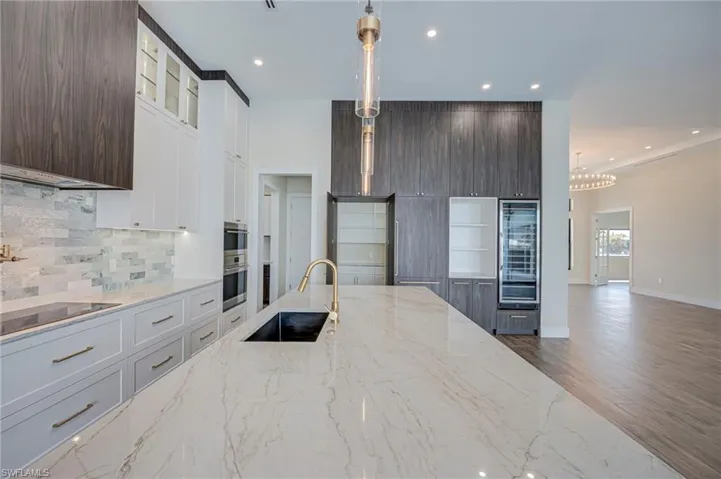Kitchen with light stone counters, glass insert cabinets, dark wood finished floors, white cabinetry, and decorative light fixtures