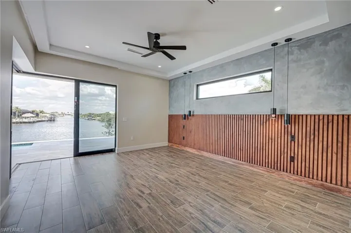 Unfurnished room with wooden walls, a raised ceiling, a ceiling fan, wood tiled floors, and a water view