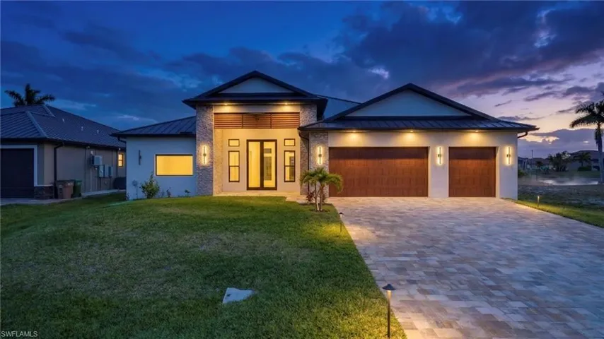 View of front of property with a standing seam roof, a garage, decorative driveway, stucco siding, and a lawn