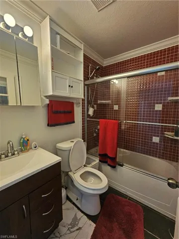 Full bathroom with crown molding, toilet, vanity, a textured ceiling, and enclosed tub / shower combo