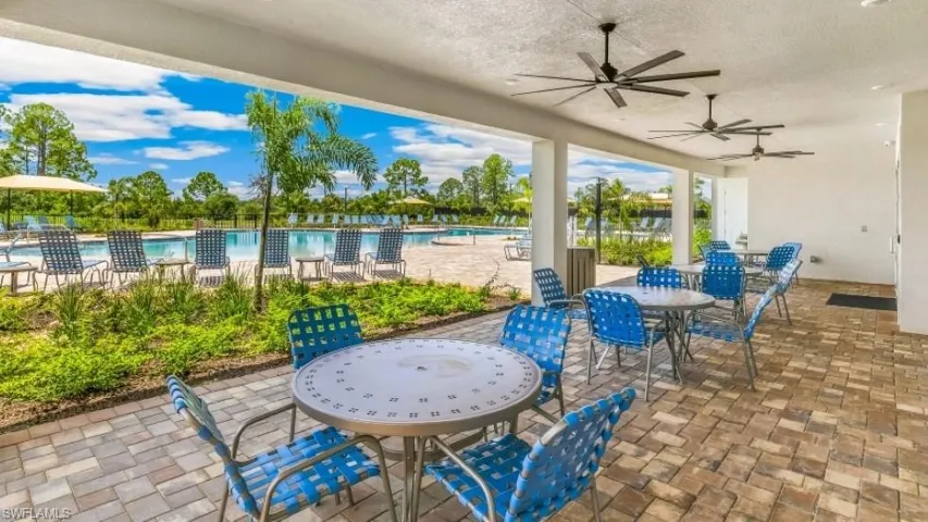 Resort-style pool area with an expansive paver deck, multiple lounge chairs, and a covered seating area